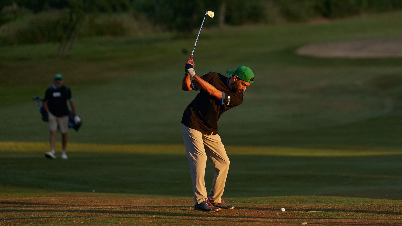 A man swings a golf club as the sun sets