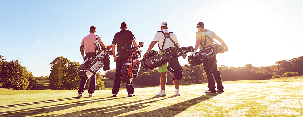 Four Golfers stand with their back to the camera looking out over the fareway, golf bags over their backs